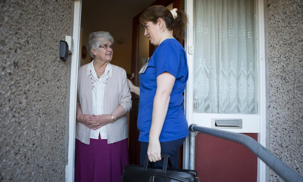 A district nurse in uniform at the front door of a patient